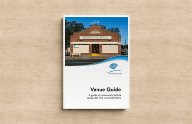 A copy of the Inverell Venue Guide, featuring the Ashford Memorial Hall on the front page, sitting on a wooden tabletop. 